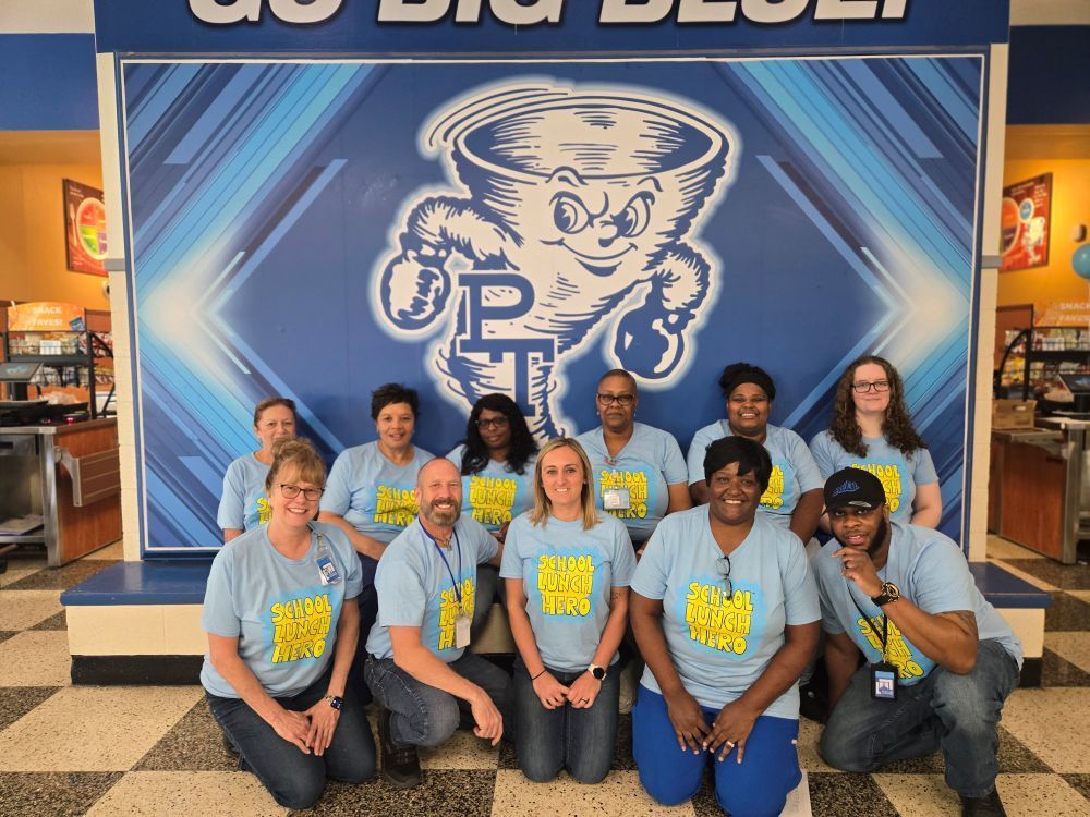 A group of people in matching blue shirts pose for a photo in front of a blue backdrop with a cartoon mascot.