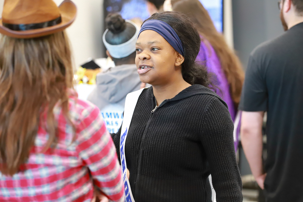 A woman with a blue headband stands among several people in an indoor area.