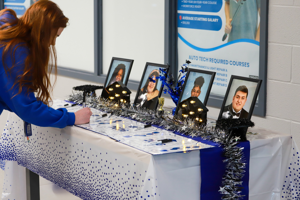 A person bends over a table with photos, lights, and decorations. A sign is behind the table.