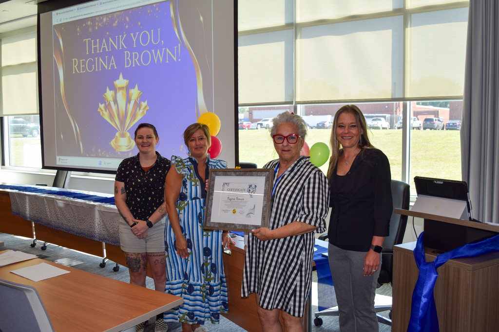 Four women stand in a room holding a plaque. One woman holds a plaque in front of her.