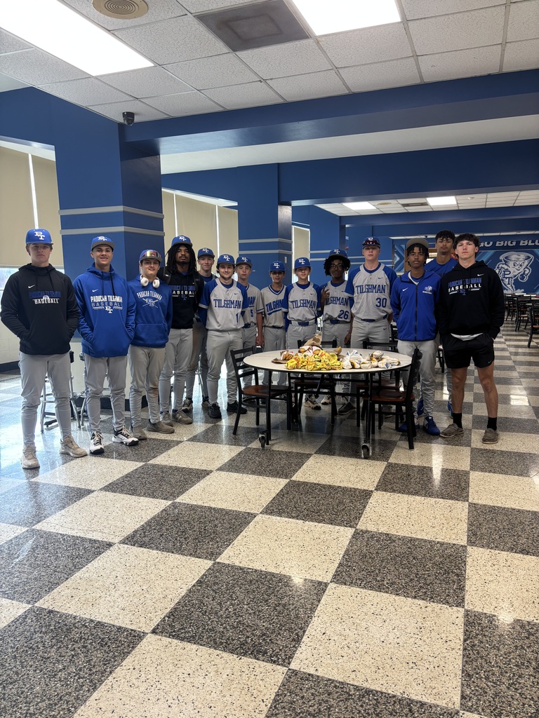 A group of young men in blue uniforms gather in a cafeteria with a checkered floor.