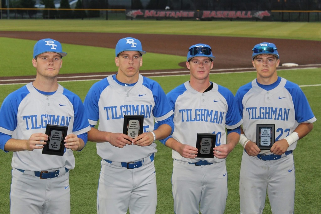 Four baseball players in blue and white uniforms hold trophies, standing on a grassy field with a blurred background.