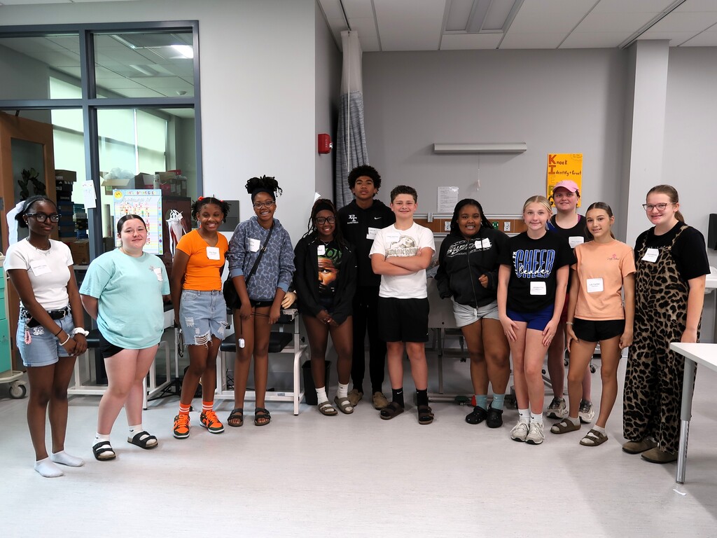 A group of young adults stands in a room, smiling and posing for a photo.