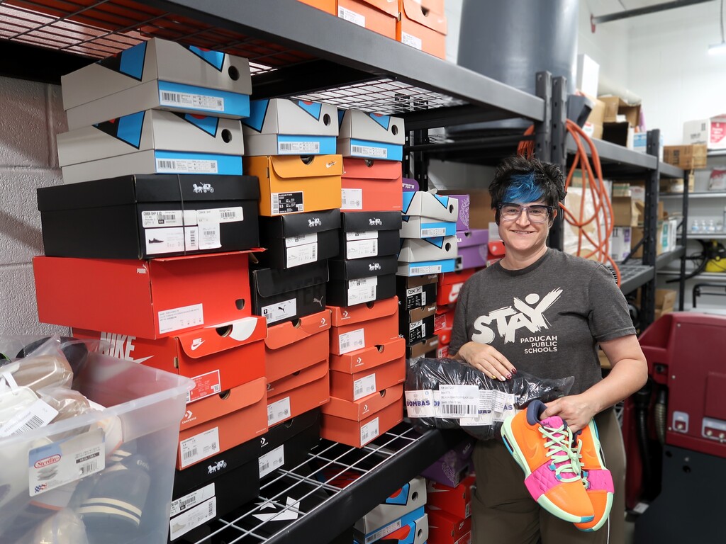 A person in a room with many stacked shoes on shelves, holding a pair of sneakers.