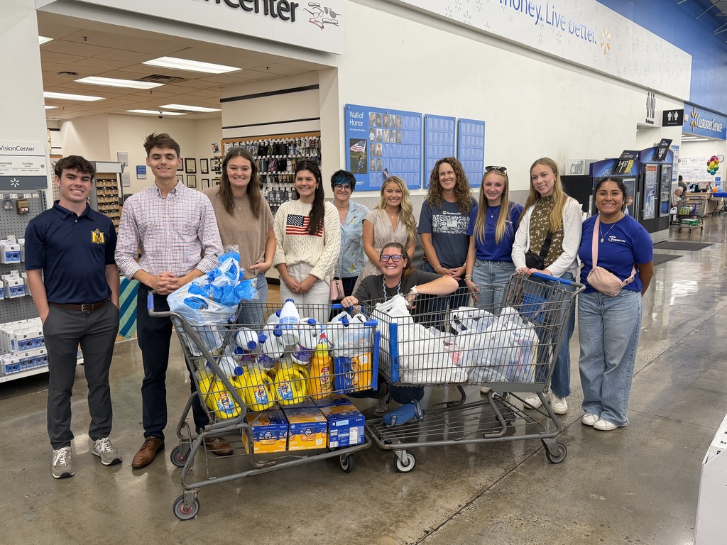 A group of people in a store with a shopping cart filled with items. They are posing for a photo.
