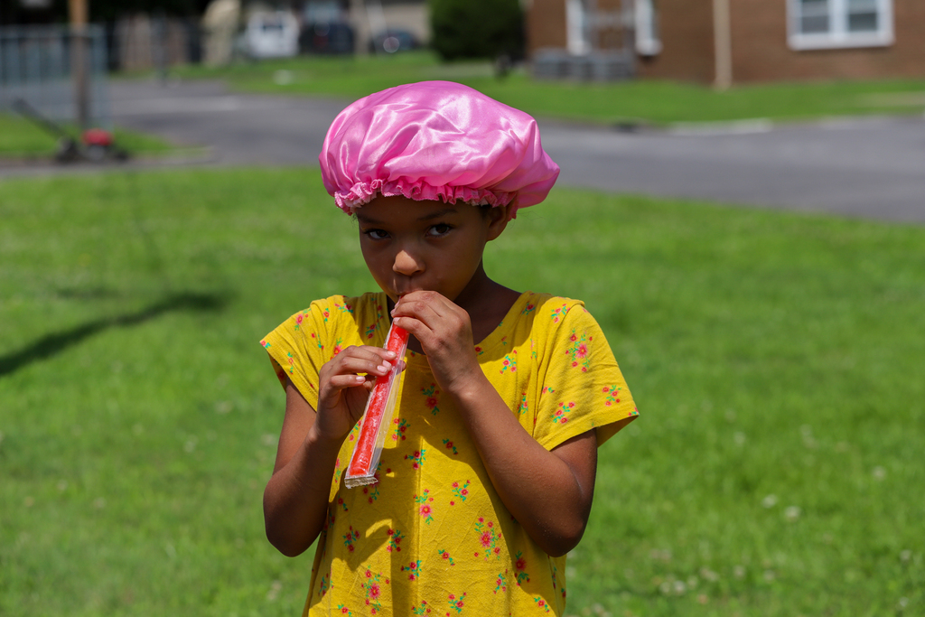 A young girl in a yellow shirt plays a harmonica while standing on a grassy field.