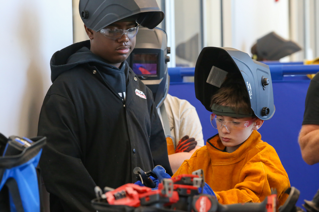 People in a workshop with safety gear on, one using a welding tool and another standing.