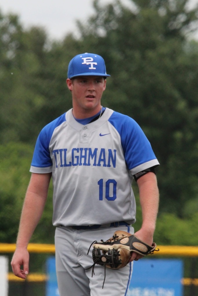 Player in baseball uniform walks on a field. Name "Tilghman" and number "10" on the jersey. Cap with letters "BT". Trees in the background.