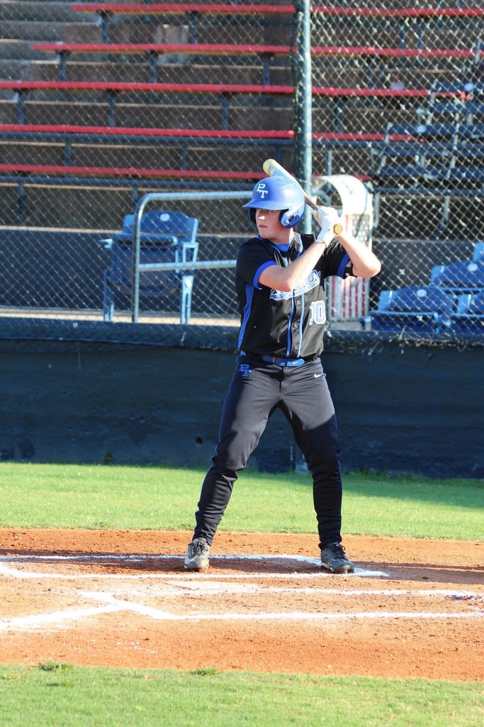 A person holding a baseball bat stands on the field, wearing a helmet, gloves, and a uniform.