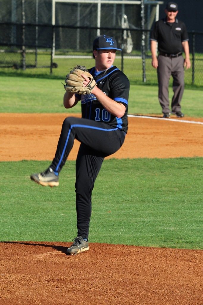 A baseball pitcher winds up on the mound, ready to throw the ball, with an umpire in the background.