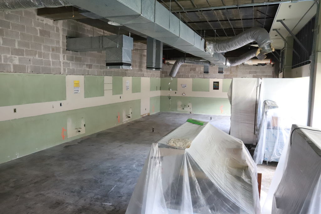 A room under construction with unfinished brick walls and green and white painted walls. A table is covered in plastic.