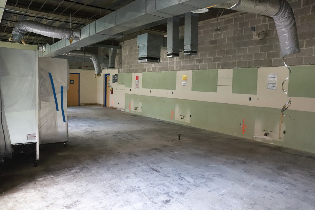 An empty room with brick walls, ducts on the ceiling, and equipment covered in tarps. One wall is green, another white.