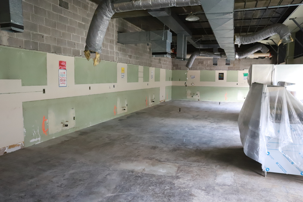 An unfinished room with green walls, gray floor, exposed brick walls, and a plastic-covered item in the corner.