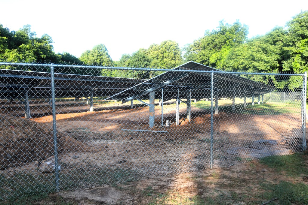 Solar panels under construction in an outdoor area surrounded by a chain-link fence and trees.