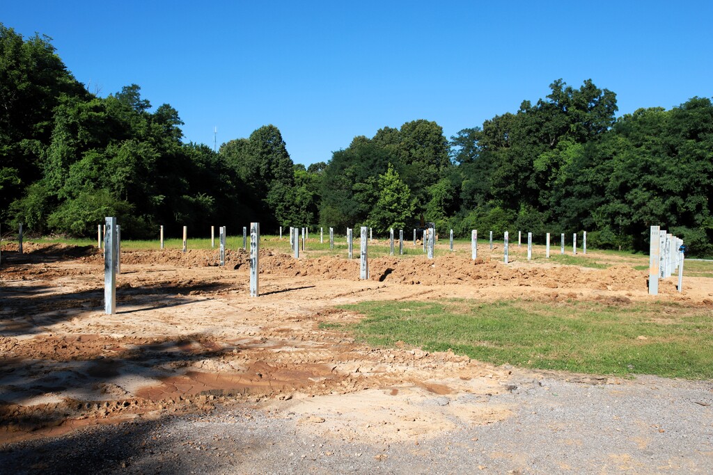 An open area with dirt ground and posts, surrounded by trees and grass under a clear blue sky.