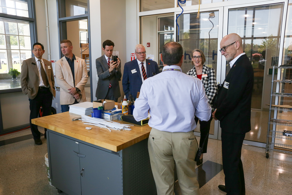 A group of adults in suits are inside a building, with one person standing behind a wooden table.