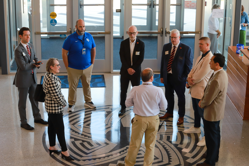 Group of people in business attire standing in a circular pattern in a lobby. They are conversing.
