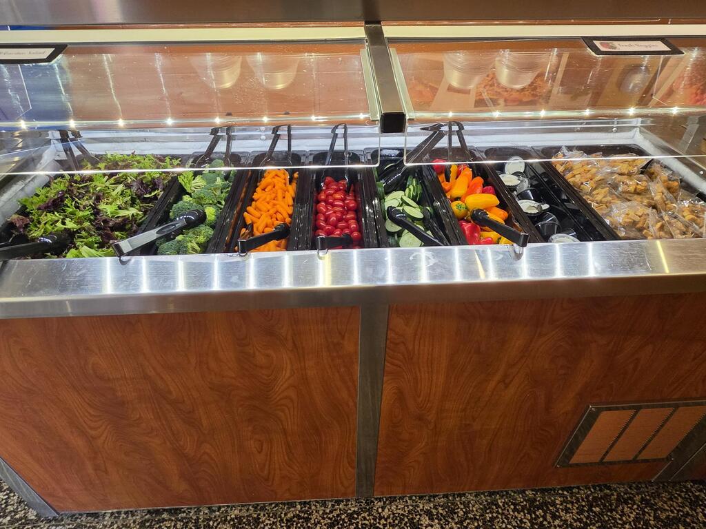 Display case with several salad sections including lettuce, carrots, and tomatoes. Glass top with metal handles.