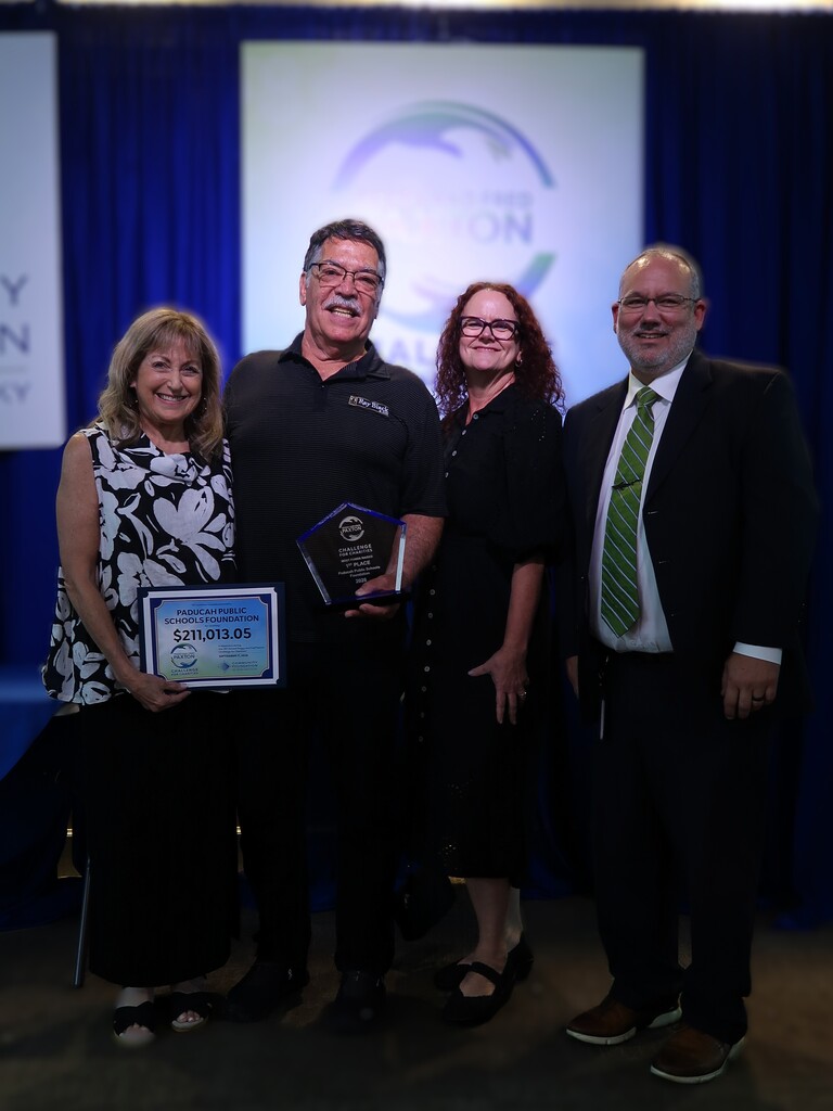 Four people pose for a photo on a stage, holding awards. Behind them is a blue curtain with a white screen.