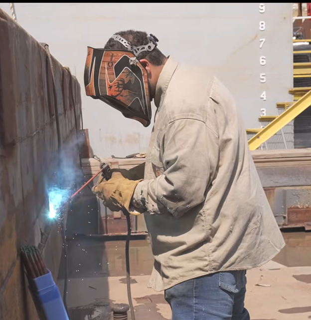 Person in a mask welding a wall. Numbers 8, 7, 5, and 3 visible in upper right corner.
