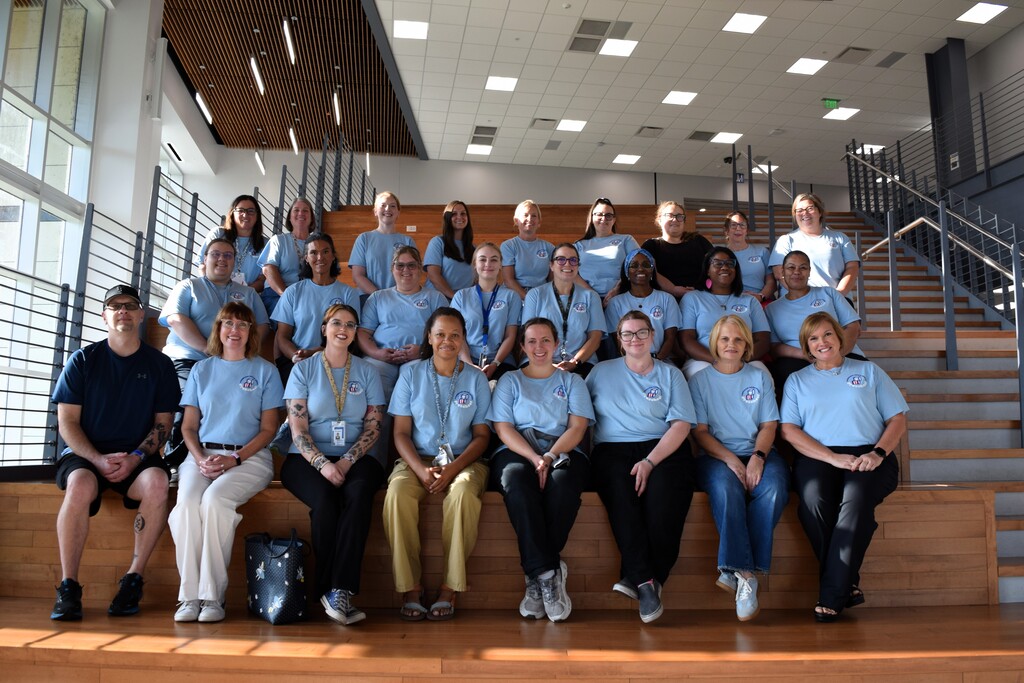 A group of individuals wearing matching blue shirts pose for a photo in a modern building with wooden benches.
