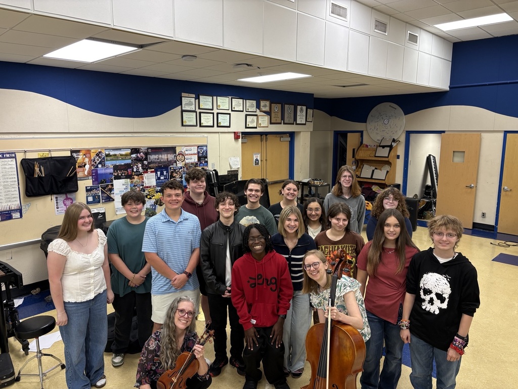 Group of students and adults posing for a picture with instruments in a music room.
