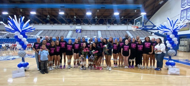 Group of young athletes in pink t-shirts standing on a basketball court with balloons.