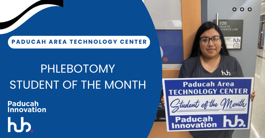 A woman wearing glasses stands in front of a blue sign that says "Phlebotomy Student of the Month".