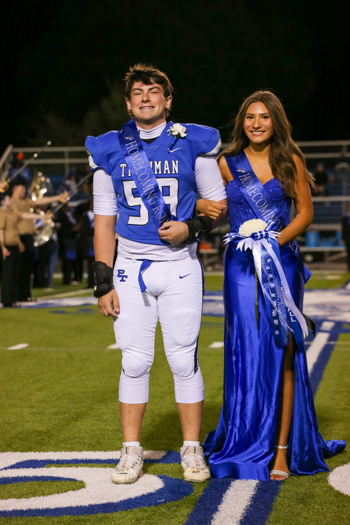 A football player in uniform and a young woman in a blue dress stand on a football field.