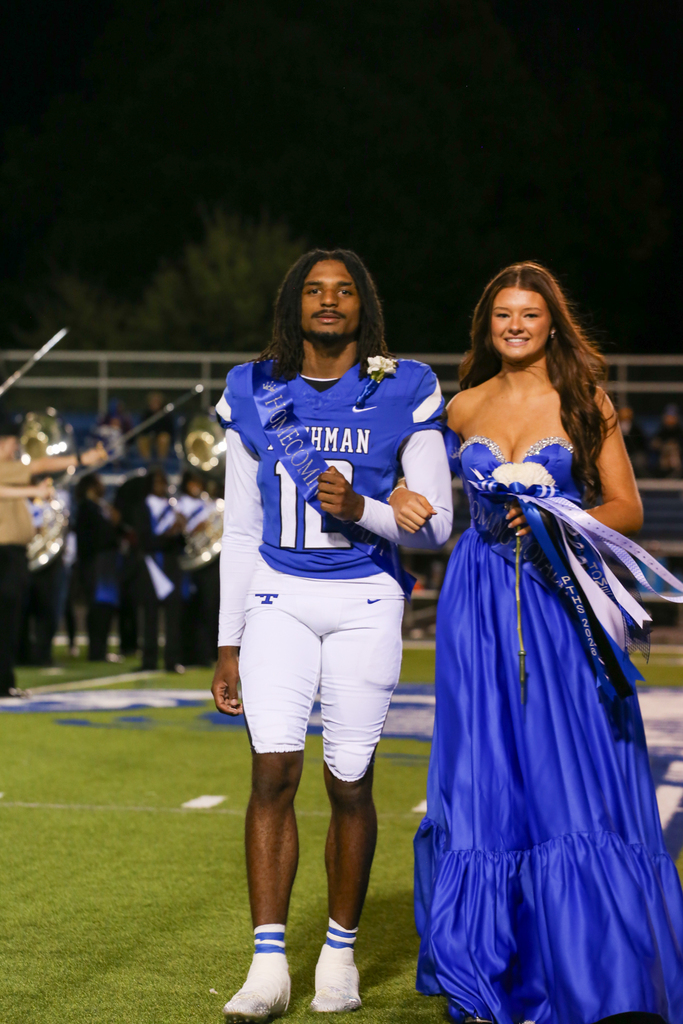 Two people on a field, one wearing a football jersey, the other wearing a blue dress.
