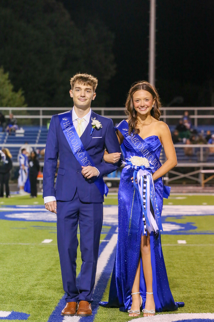 Boy in suit and girl in dress standing on a football field, smiling and posing for a photo.