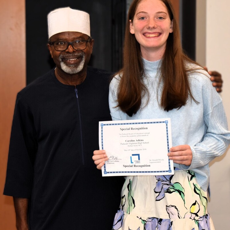 Person wearing a white hat holds paper certificate with person wearing long dress with flowers on it.