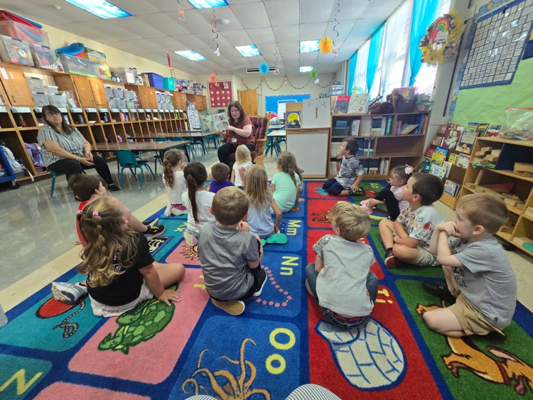 A group of smiling students gathers around a friendly black dog during a classroom visit.