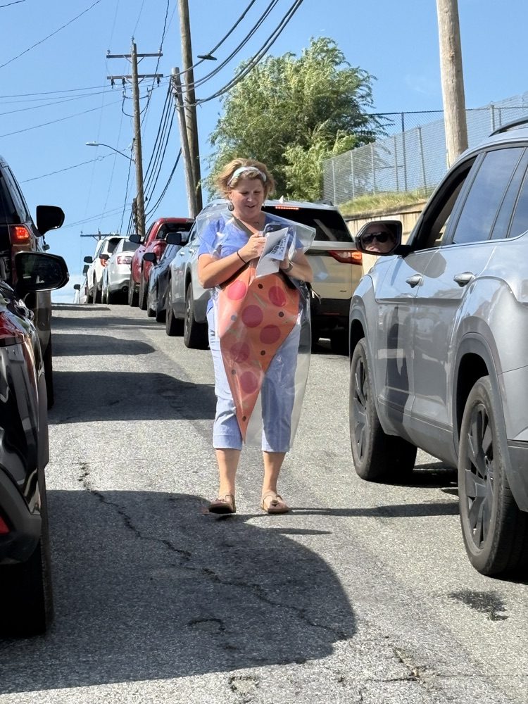 A Shenandoah Elementary staff member wearing a pepperoni pizza-slice costume walks between cars while promoting the Mamma Mia’s fundraiser.