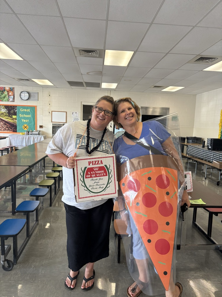 Two smiling Shenandoah Elementary staff members pose in the cafeteria. One holds a pizza box while the other wears a large pepperoni pizza-slice costume to promote the Mamma Mia’s fundraiser.