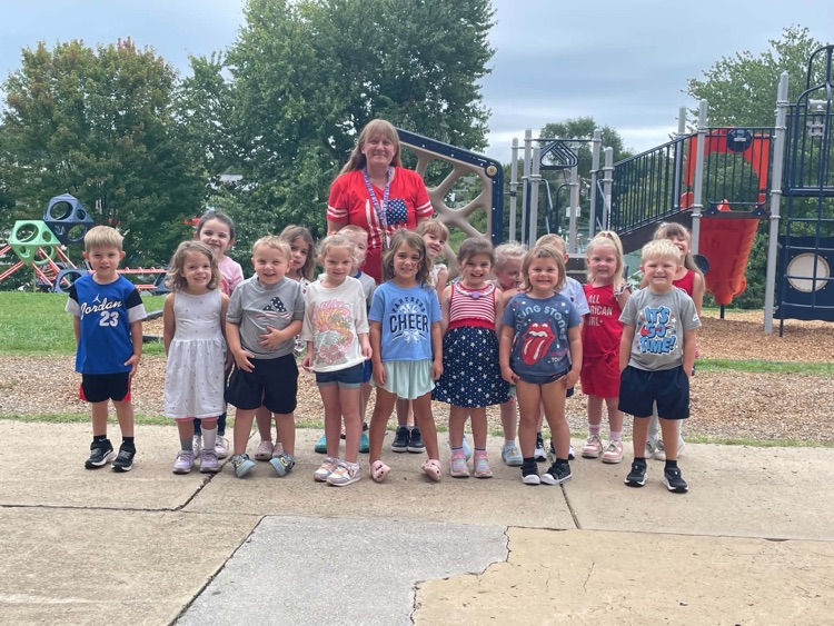 A preschool teacher and her students pose together on the playground while wearing red, white, and blue for Patriot Day