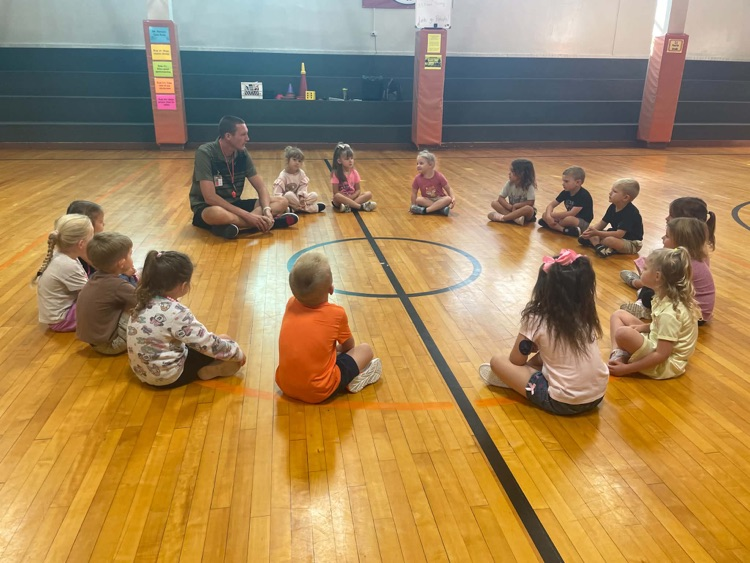 Pre-k students sit in circle with PE teacher in the gym.