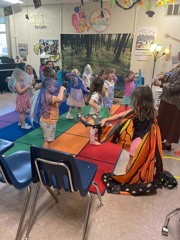 Pre-k students parented to be butterflies as the sing and dance while the music teacher plays an instrument.