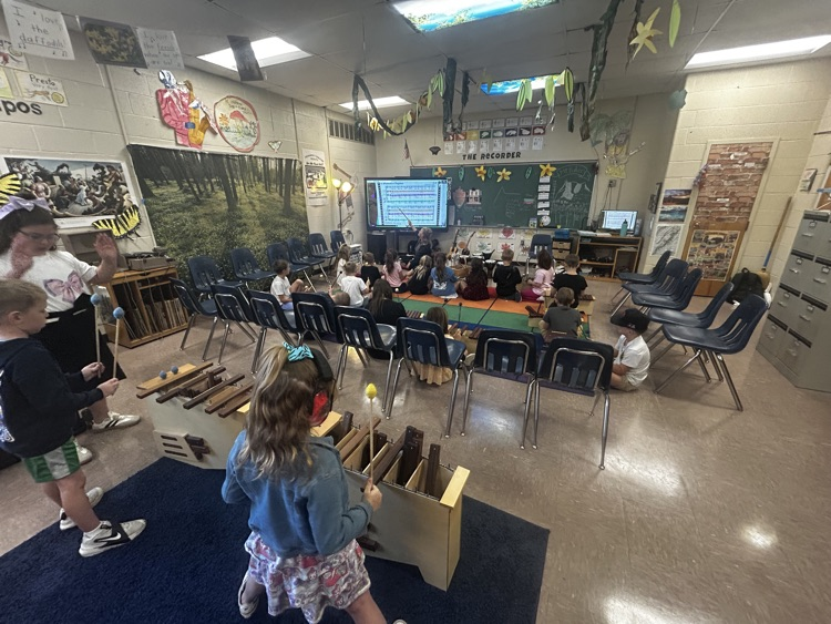     Students play xylophones while classmates sit on the rug near the teacher.