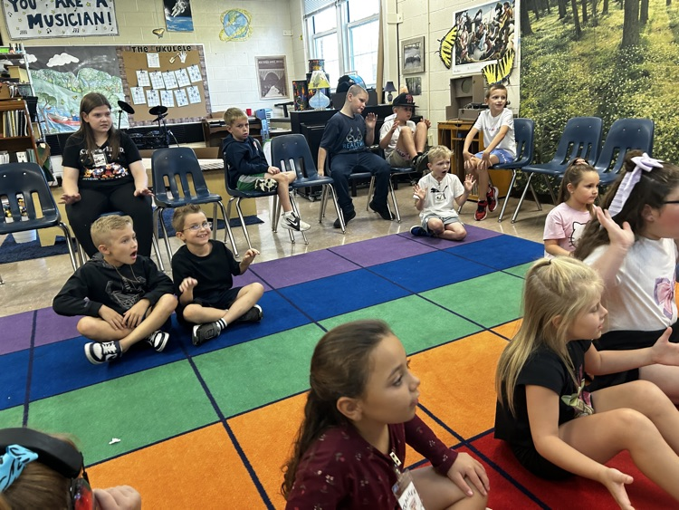     Students participate with hand motions while seated during music class.