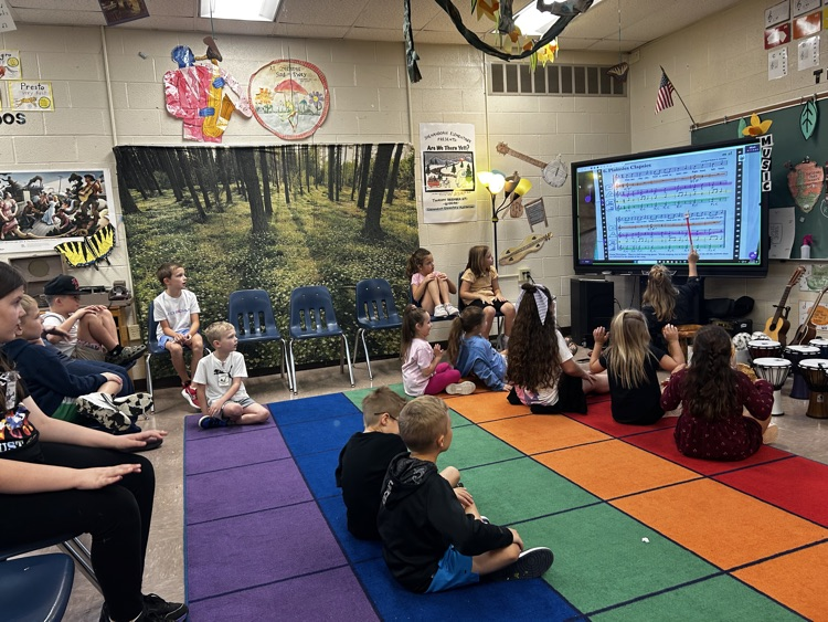     Students follow along as the teacher points to sheet music displayed on the classroom screen.