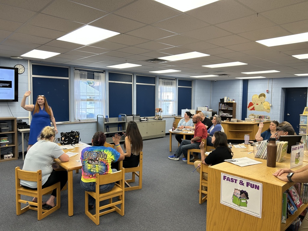 Families seated around tables in the school library participate in a SPARK 360 parent workshop while a presenter leads the discussion from the front of the room.