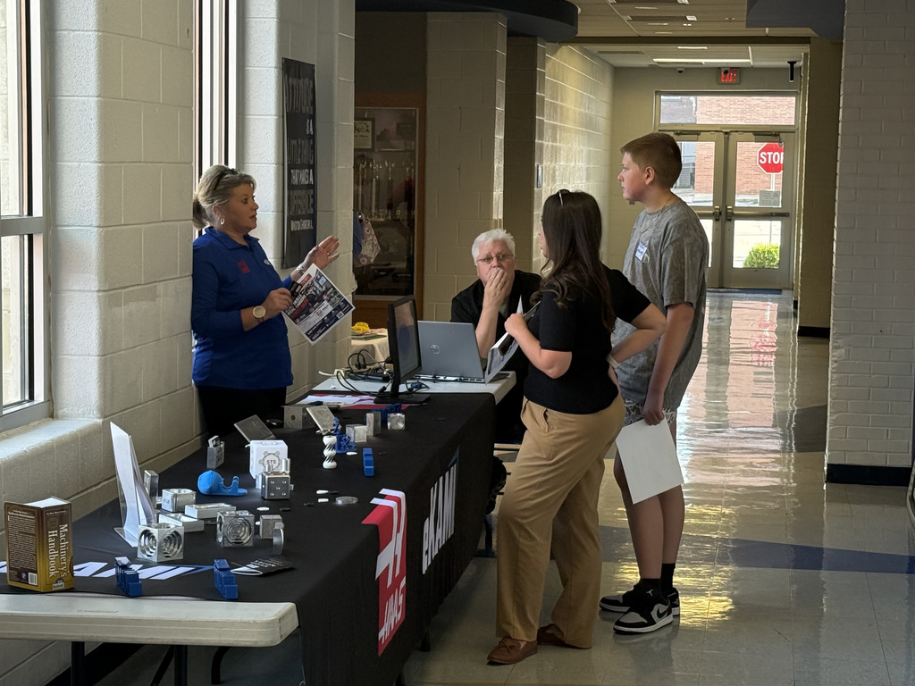 A student and family members talk with a community partner at a resource table displaying information and materials during SPARK 360 Family Transition Night.