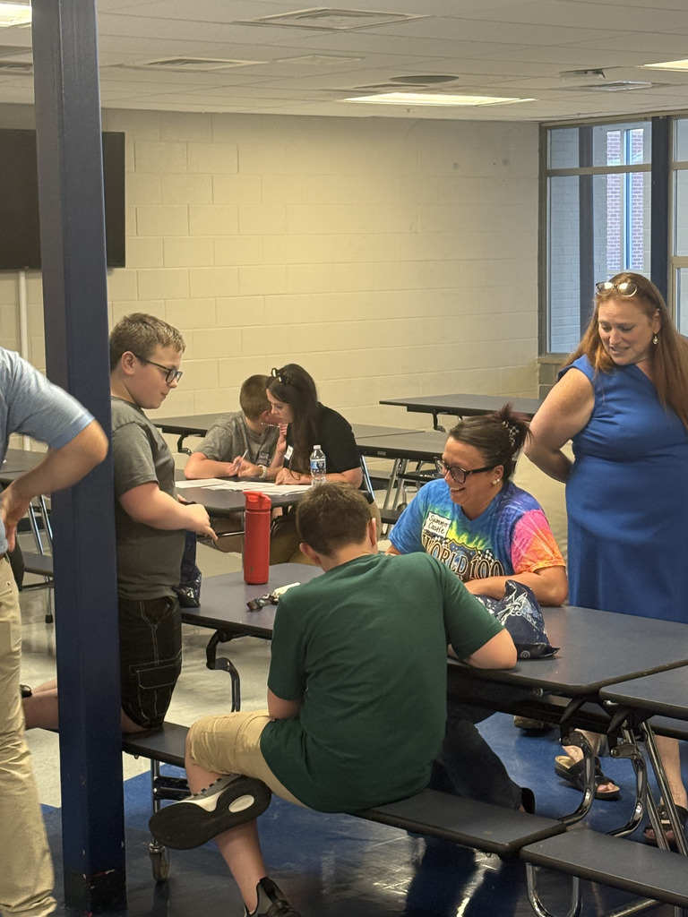 Students and adults gathered around a table during SPARK 360 Family Transition Night, smiling and talking together during an interactive activity.