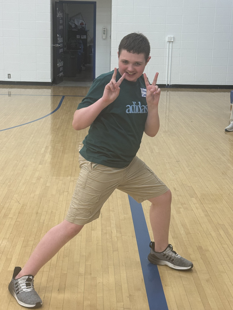 A smiling student poses playfully with both hands making peace signs in the school gym during SPARK 360 Family Transition Night.