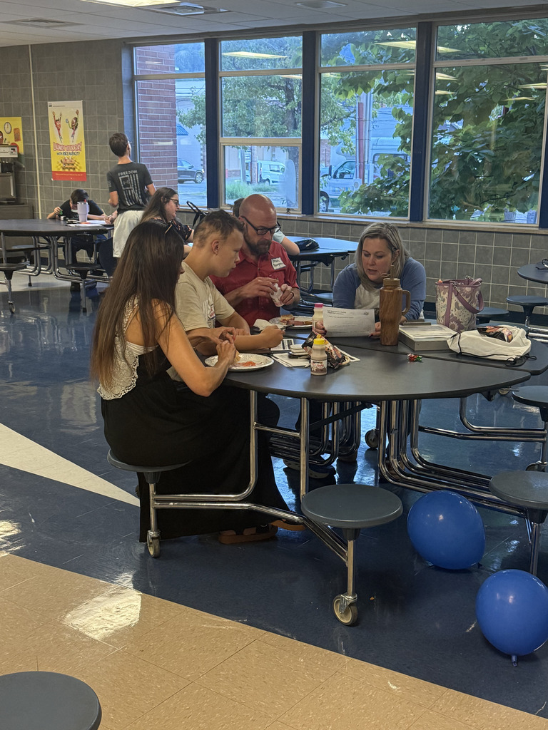 Students and family members sit together around a cafeteria table reviewing printed information and discussing transition planning.