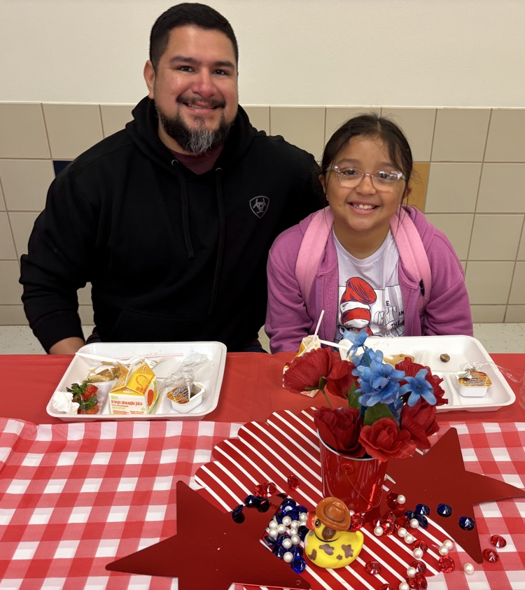 Parent with student at table with red and white checkered table cloth eating breakfast 