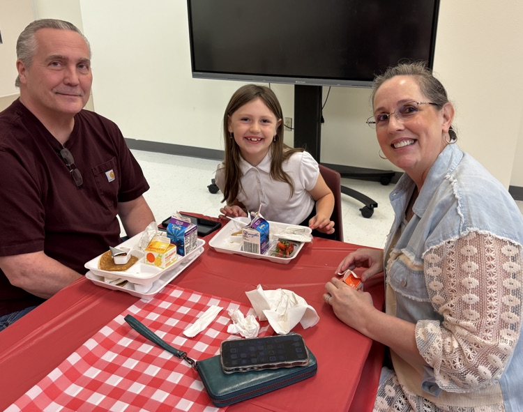 Parent with student at table with red and white checkered table cloth eating breakfast