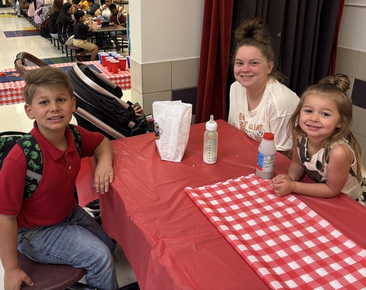 Parent with student at table with red and white checkered table cloth eating breakfast