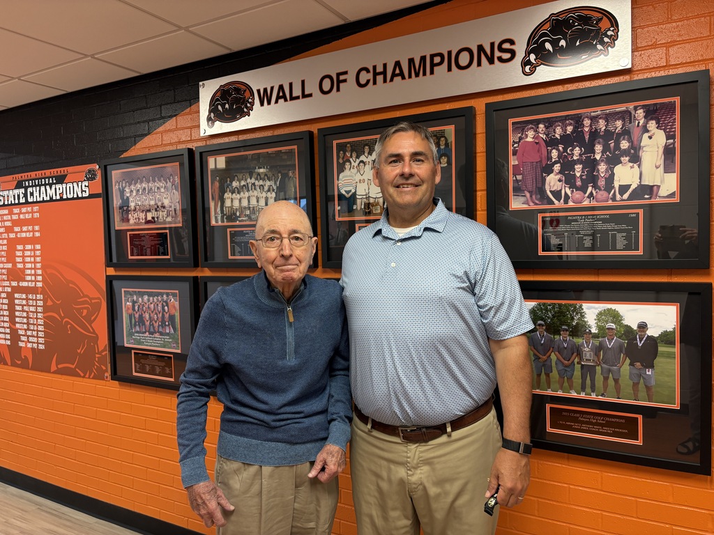 Mr Lenzini and Mr Harper standing in front of Wall of Champions